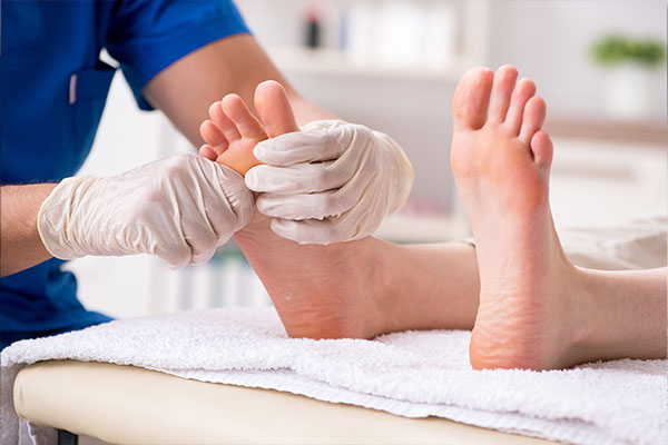 A medical professional is performing a foot treatment on a patient s barefoot, with both feet elevated and the practitioner wearing gloves.